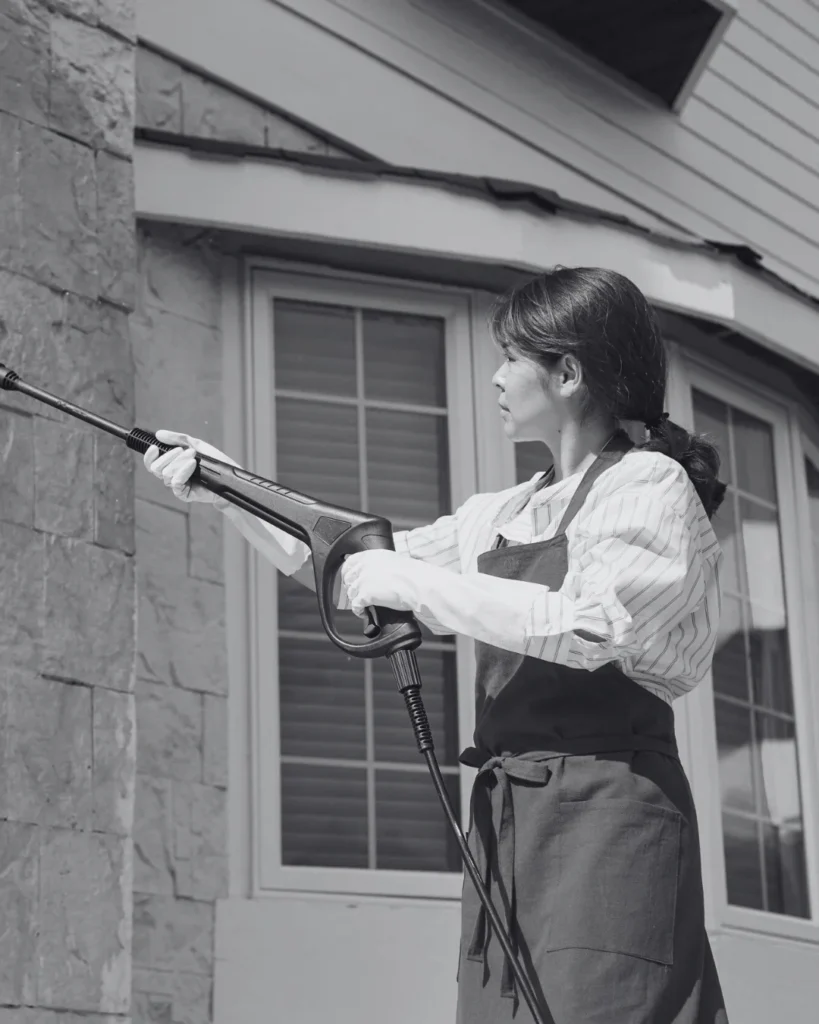 This image shows a woman cleaning the house wall with a pressure washer